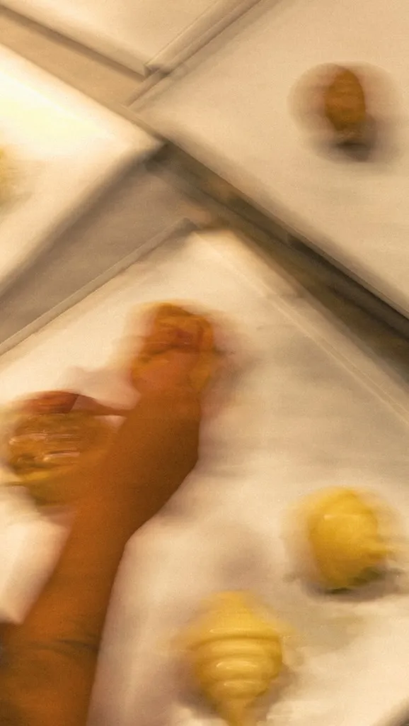 Mãos da casa moldando croissants em assadeiras, no ritmo da fornada